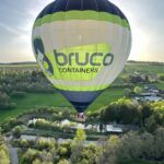 Luchtballon met het bedrijfslogo van Bruco die elegant over het landschap vaart tijdens een vlucht met Filva Ballonvaarten